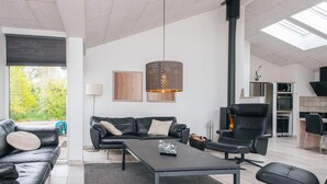 A modern living room with a sofa, coffee table, and chairs, a fireplace, and a kitchen area. - 5 Star Holiday Home in Henne (Henne)