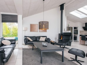 A modern living room with a sofa, coffee table, and chairs, a fireplace, and a kitchen area.