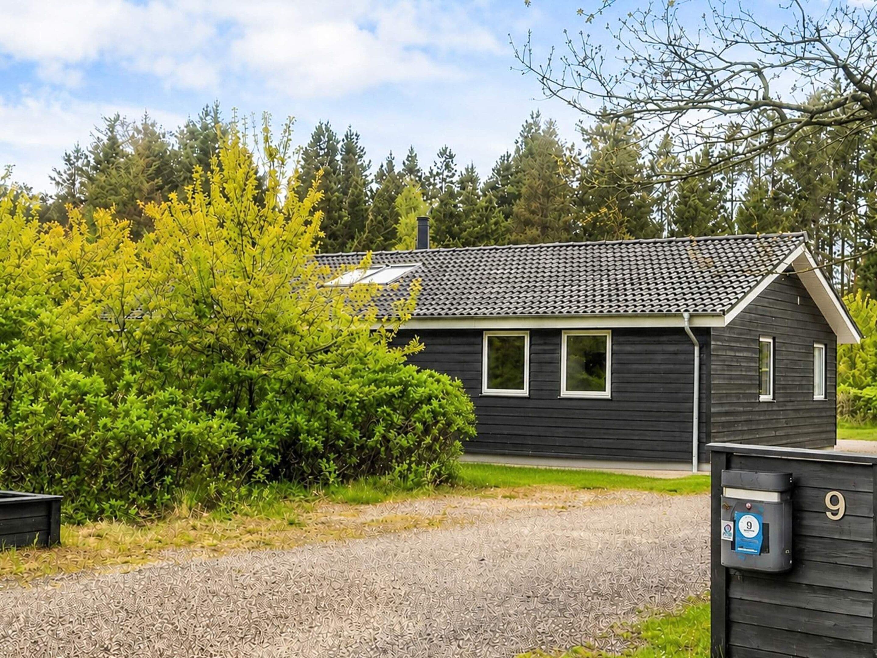 En etagers bygning med mørk facade, et tegltag og en grusvej.