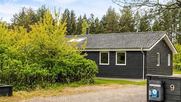 En etagers bygning med mørk facade, et tegltag og en grusvej.