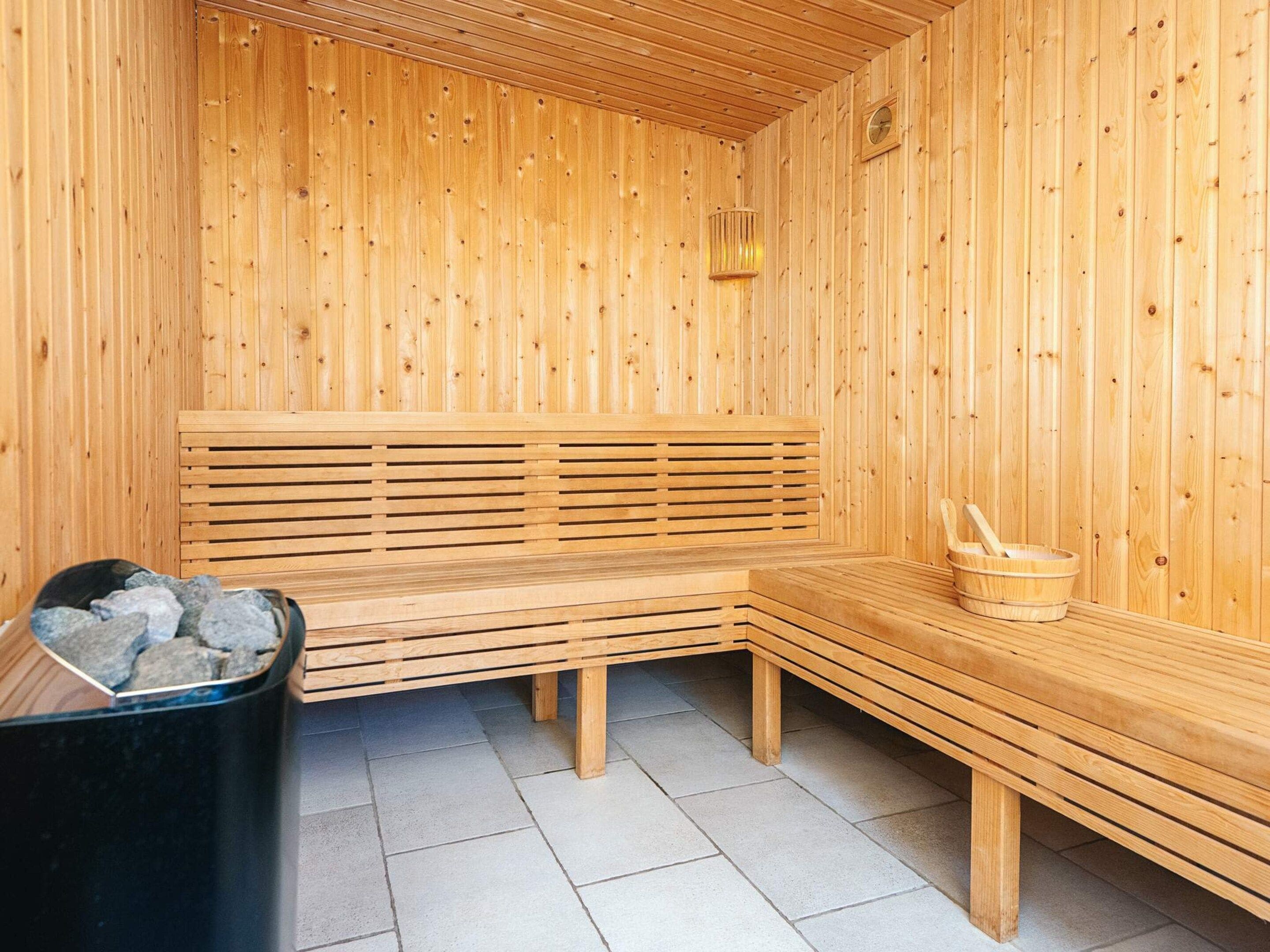 A wooden sauna with benches, a stone basin, and a wooden bucket.