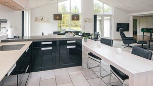 A modern kitchen with a central island, black cabinetry, and a dining area with a long table and chairs. - 5 Star Holiday Home in Henne (Henne)