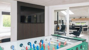 A modern office space with a foosball table, a flat-screen TV, and a kitchen area. - 5 Star Holiday Home in Henne (Henne)