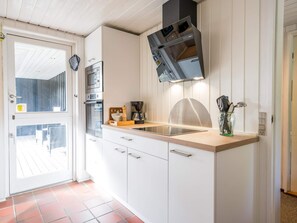A modern kitchen with white cabinetry, a stainless steel range hood, a built-in oven, and a coffee maker.