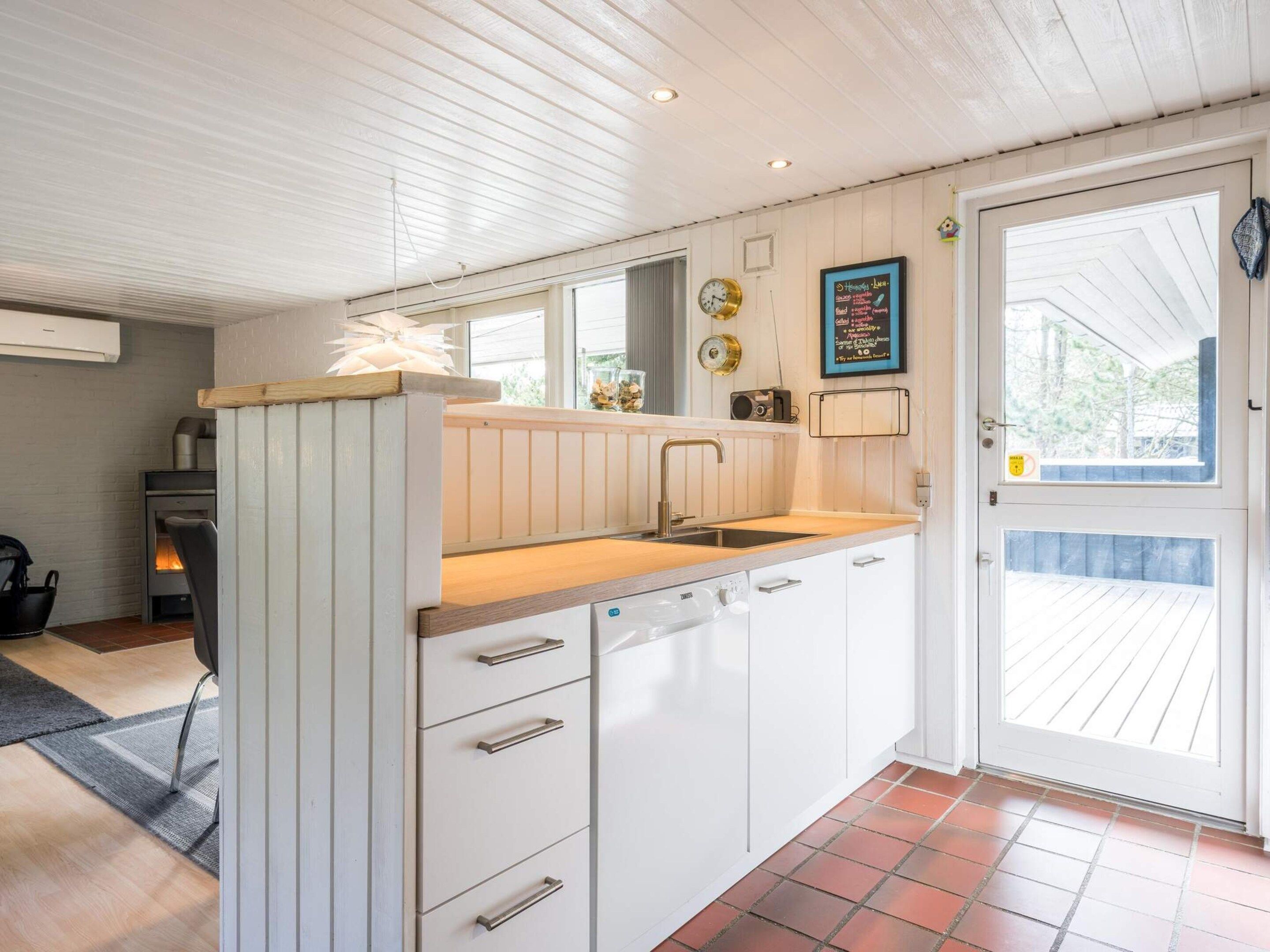 Une cuisine compacte avec des meubles blancs, un plan de travail en bois et un lave-vaisselle encastré.