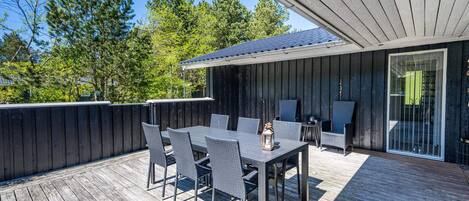 An outdoor patio with a table and chairs, a covered seating area, and a view of trees and a building in the background.