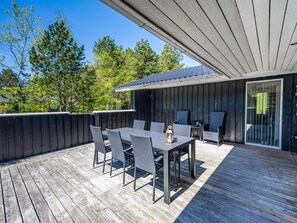 An outdoor patio with a table and chairs, a covered seating area, and a view of trees and a building in the background.