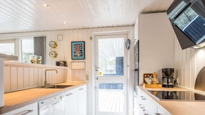 A compact kitchen with white cabinets, a wooden countertop, a built-in dishwasher, and a coffee maker. - 4 Star Holiday Home in Norre Nebel (Norre Nebel)