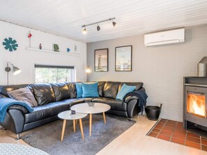 A modern living room with a leather sofa, a round coffee table, a fireplace, and a large window.