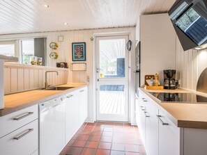 A compact kitchen with white cabinetry, a wooden countertop, a coffee maker, and a window with a view. - 4 Star Holiday Home in Norre Nebel (Norre Nebel)