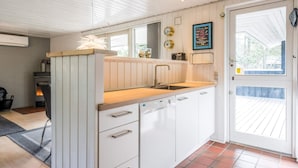 A compact kitchen with white cabinets, a wooden countertop, and a built-in dishwasher. - 4 Star Holiday Home in Norre Nebel (Norre Nebel)