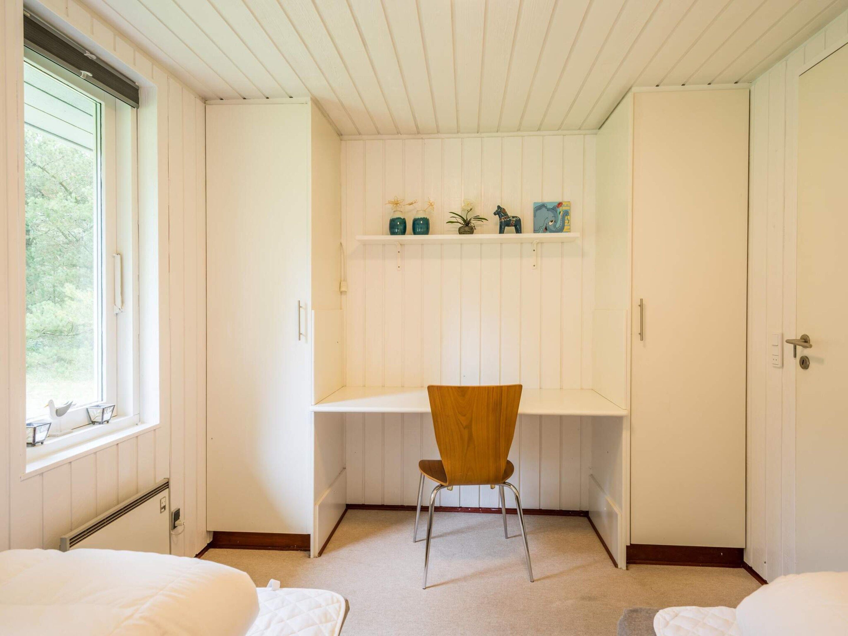 A bedroom with a single bed, a chair, a desk with shelves, and a window.