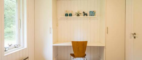 A bedroom with a single bed, a chair, a desk with shelves, and a window.