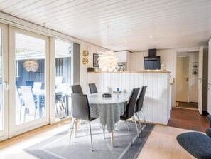 A dining area with a round table, chairs, and a kitchen area with a TV and cabinets.