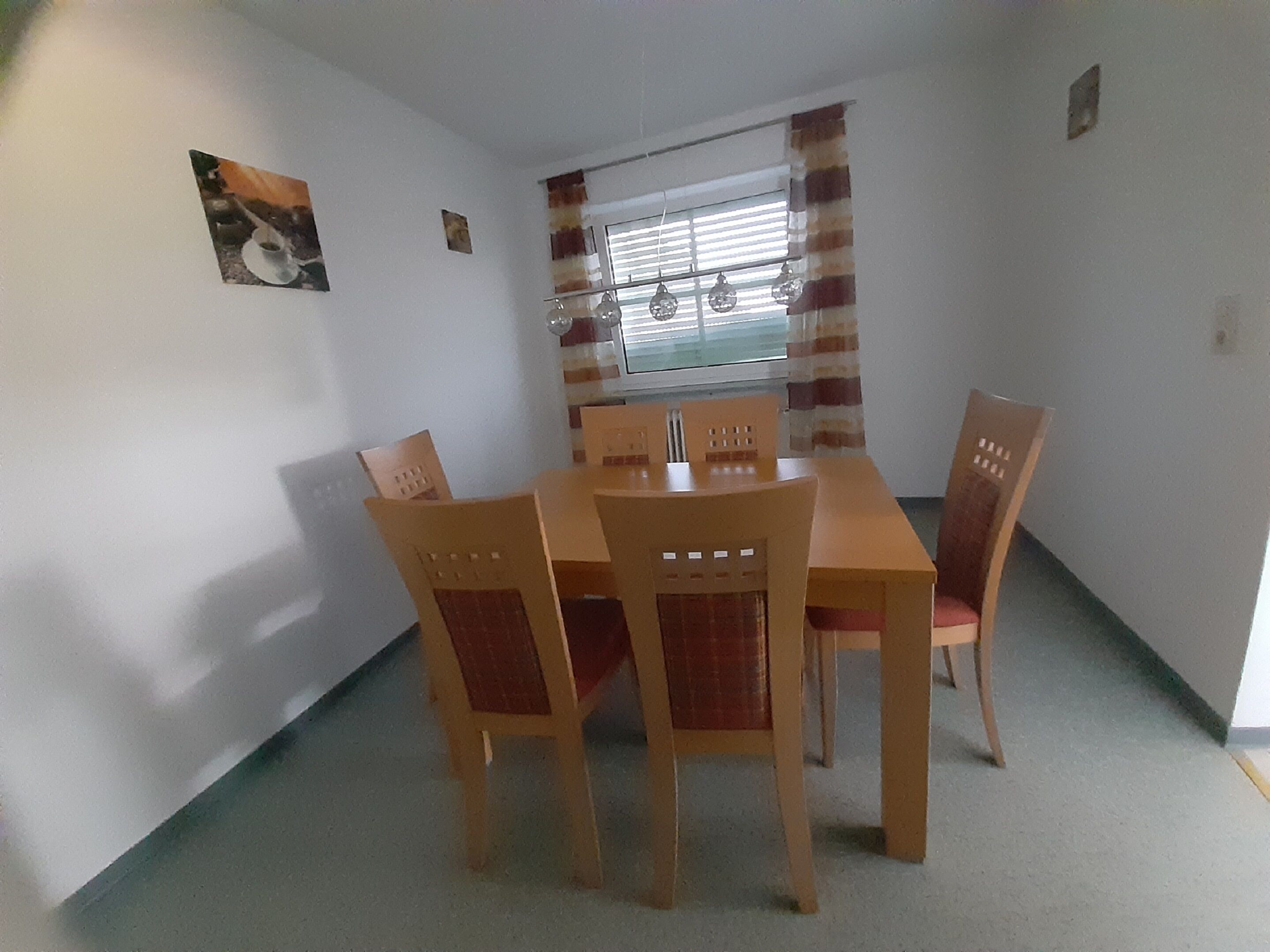 A dining area with a wooden table and four chairs, a window with blinds, and a small picture on the wall.