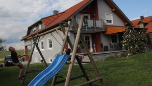 Una casa con una estructura de juego de madera, que incluye un tobogán, y un techo con tejas rojas.