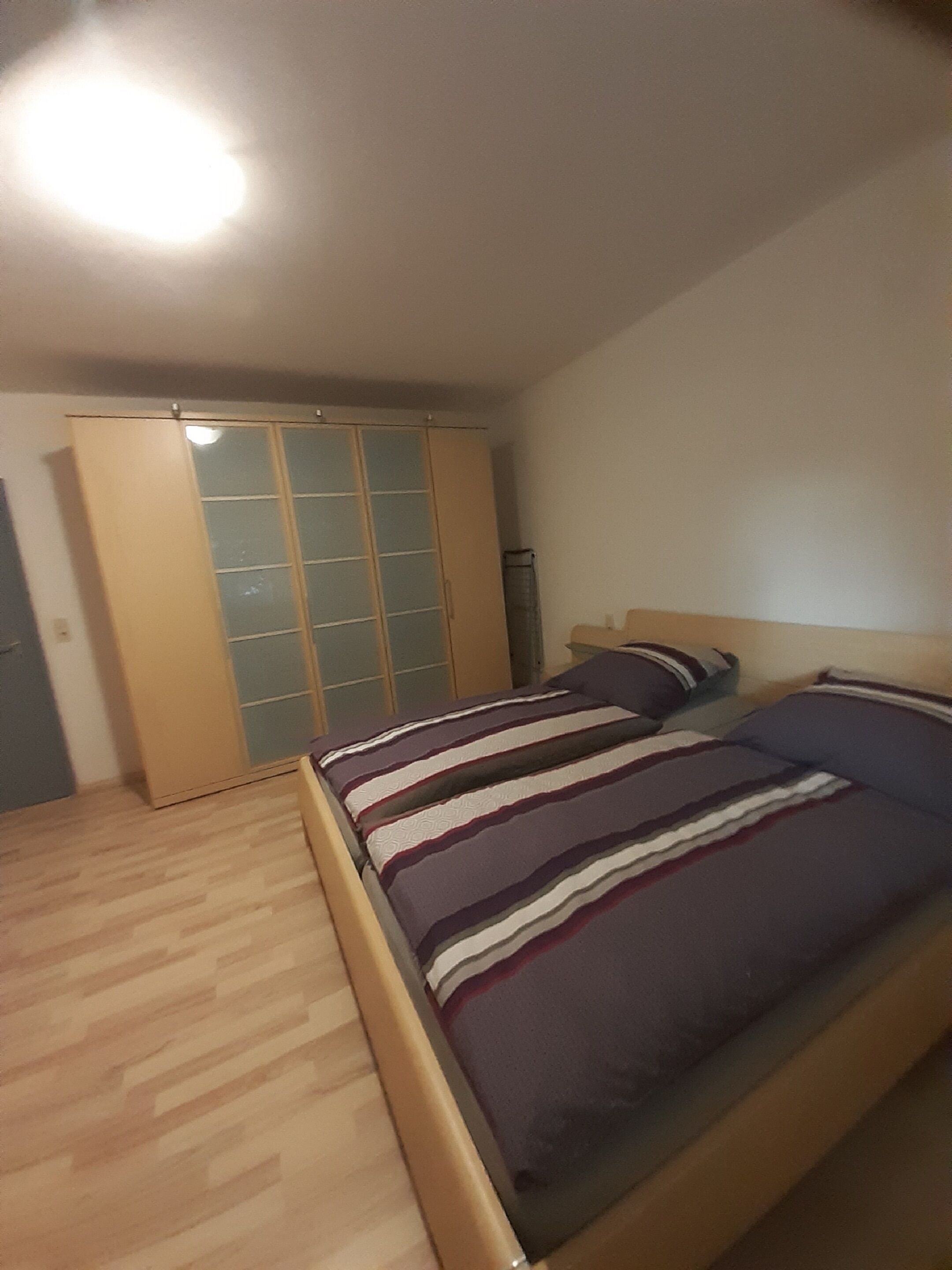 A bedroom with a bed, wooden floor, and a sliding door closet.