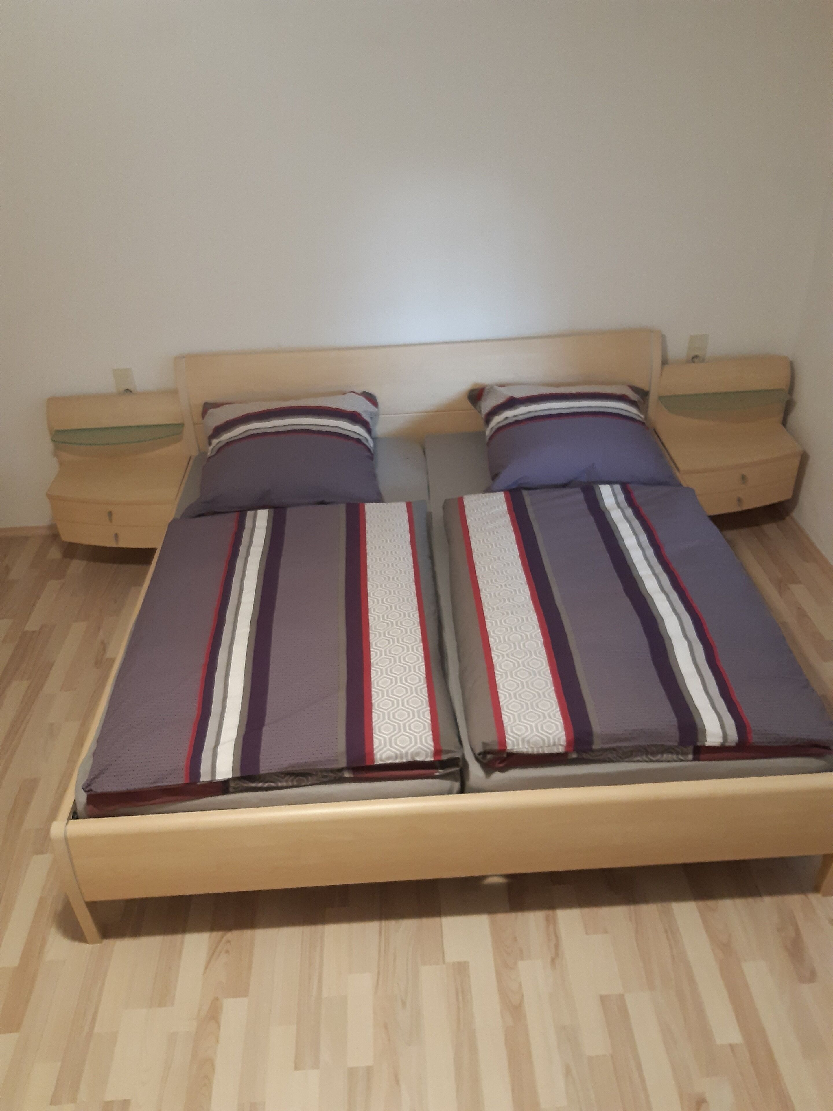 A double bed with striped bedding, two bedside tables, and a wooden floor.