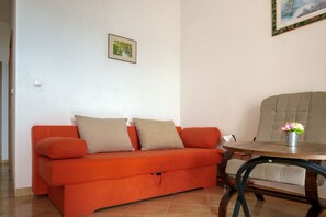 Una stanza con un divano rosso, un tavolino rotondo con un vaso di fiori e un quadro appeso al muro.