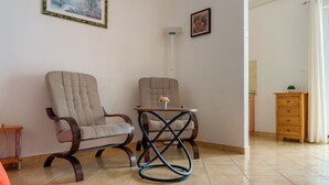A living room with two armchairs, a small table with a flower vase, a wooden cabinet, and a painting on the wall.