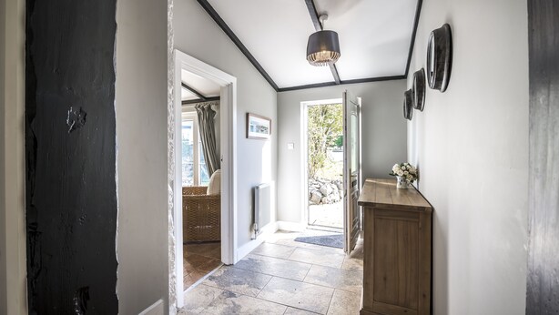 A hallway with a dark door, a wooden cabinet, and a hanging light fixture. - Barn Conversion - Hot Tub - Penally (Tenby)