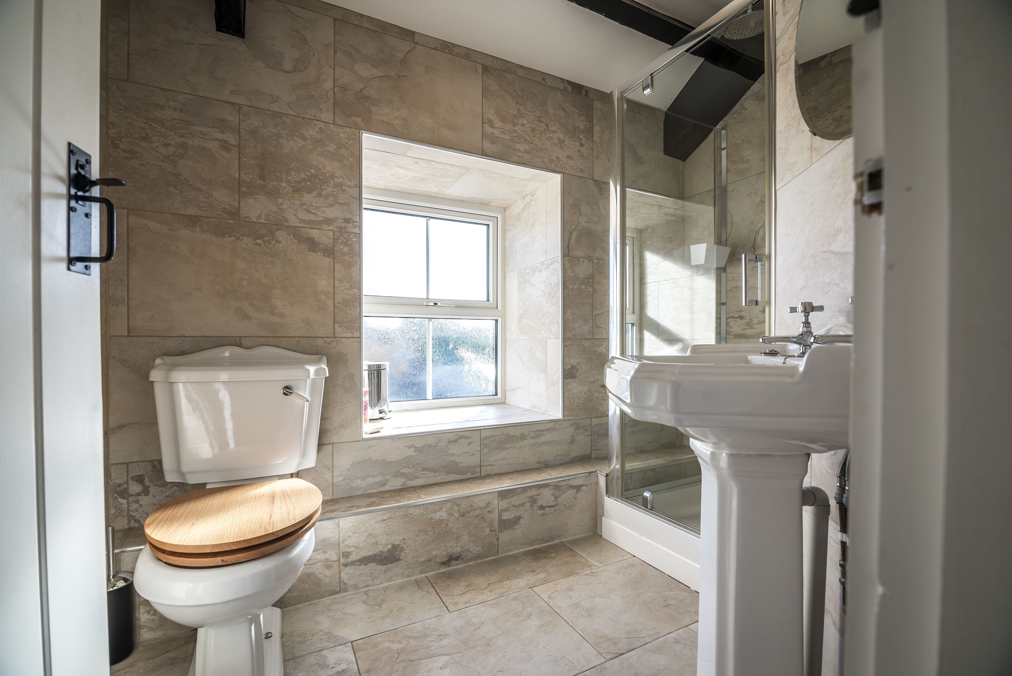 A bathroom with a toilet, a window, a shower, and a sink.