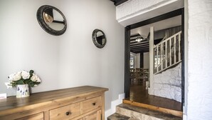 A wooden dresser with a vase of white flowers, two wall-mounted mirrors, and a stone staircase leading to a room with a white wall and a wooden ceiling. - Barn Conversion - Hot Tub - Penally (Tenby)
