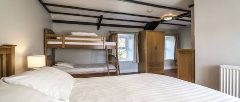 A bedroom with a large bed, a bunk bed, a wooden wardrobe, and a window with curtains.
