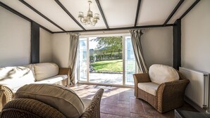 A sunlit room with a large sliding glass door leading to a garden, furnished with wicker chairs and a sofa. - Barn Conversion - Hot Tub - Penally (Tenby)