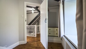 A bedroom with a wooden floor, a white bed, a white dresser, and a window with curtains. - Barn Conversion - Hot Tub - Penally (Tenby)