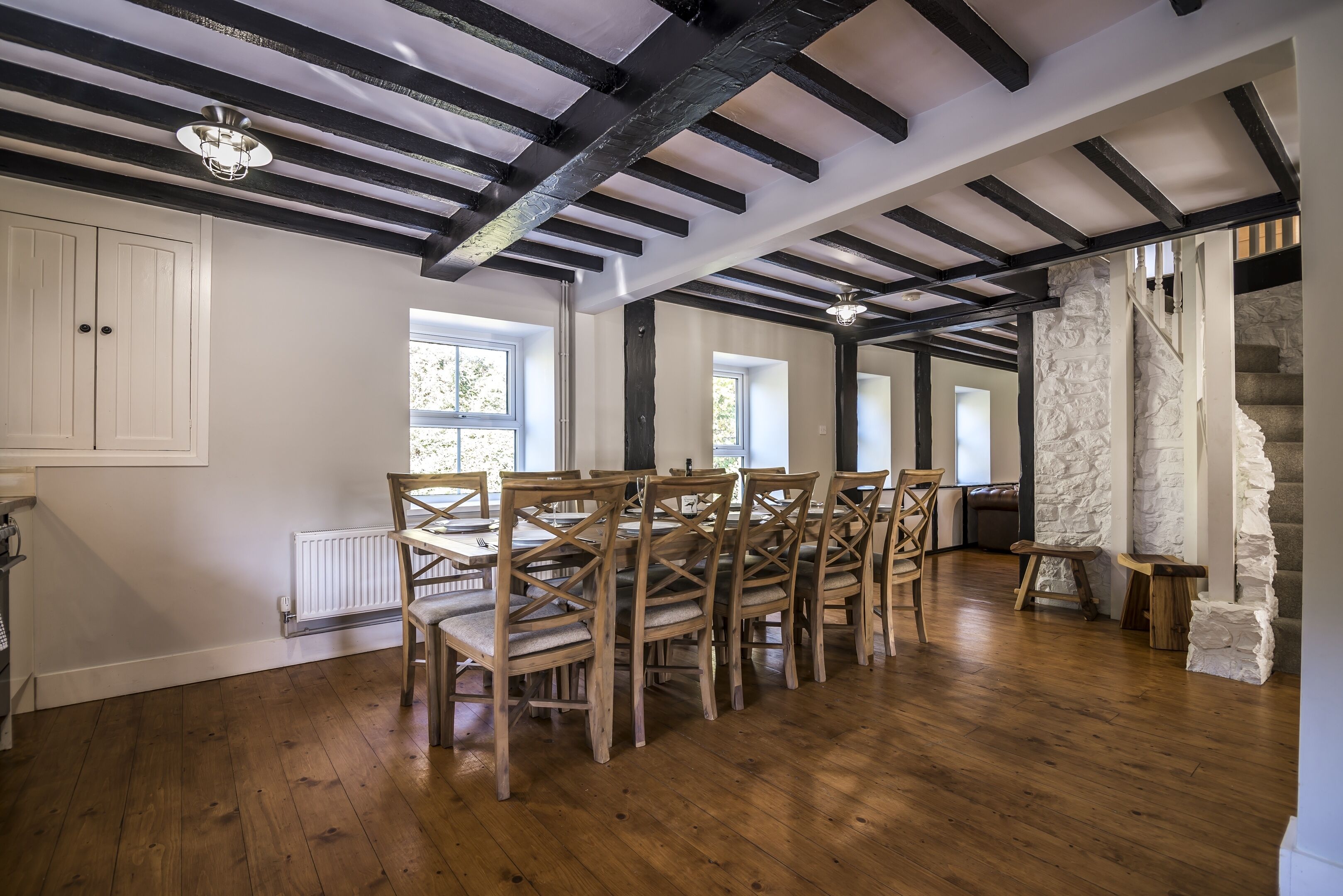 A spacious dining area with wooden chairs and a table, exposed beams on the ceiling, and a stone wall.