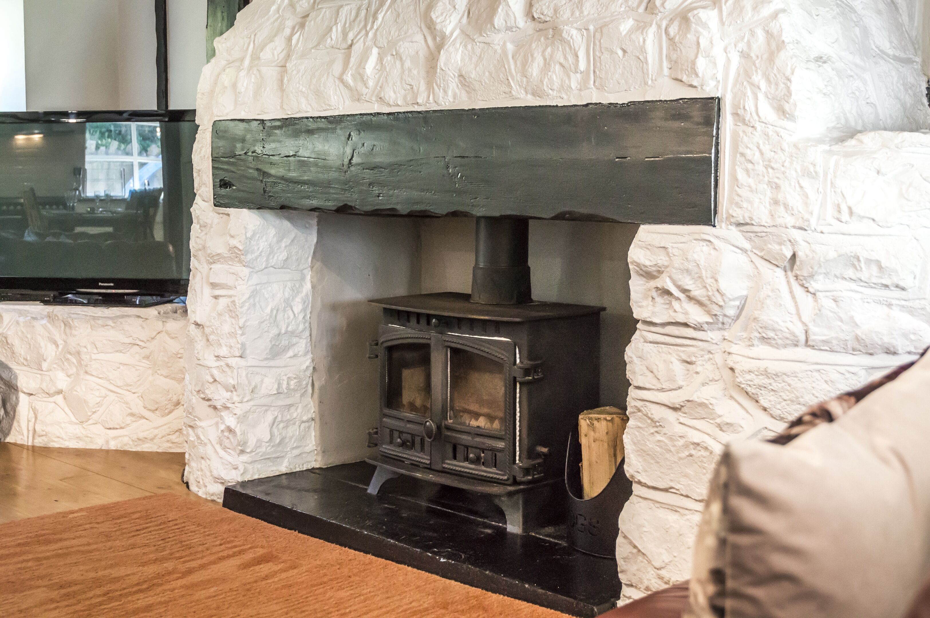 A stone wall with a black wood-burning stove and a television mounted on the wall.