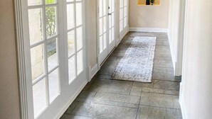 Un couloir doté de grandes fenêtres, d’un sol en pierre et d’une petite alcôve où se trouve une plante.