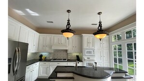 Une cuisine avec des meubles blancs, un réfrigérateur en acier inoxydable, un plan de travail en granit et deux lampes suspendues.