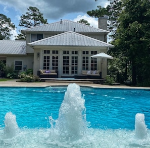 Une maison avec une piscine, une fontaine et un patio couvert avec des sièges.