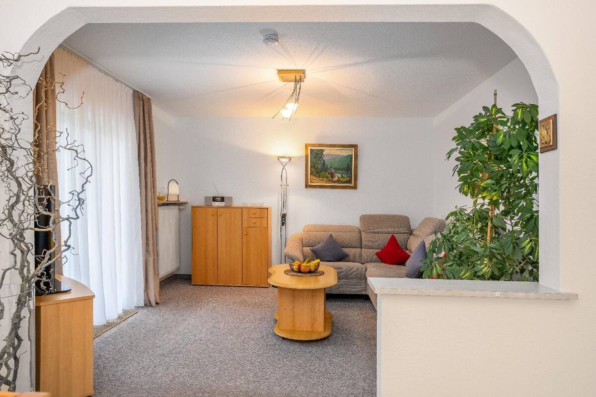 A cozy living room with a wooden cabinet, a round wooden table with fruit, a sofa with cushions, and a plant.