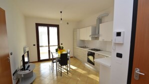 A modern kitchen with white cabinets, a gas stove, and a built-in oven. There is a dining area with a table and chairs, and a TV on a stand.