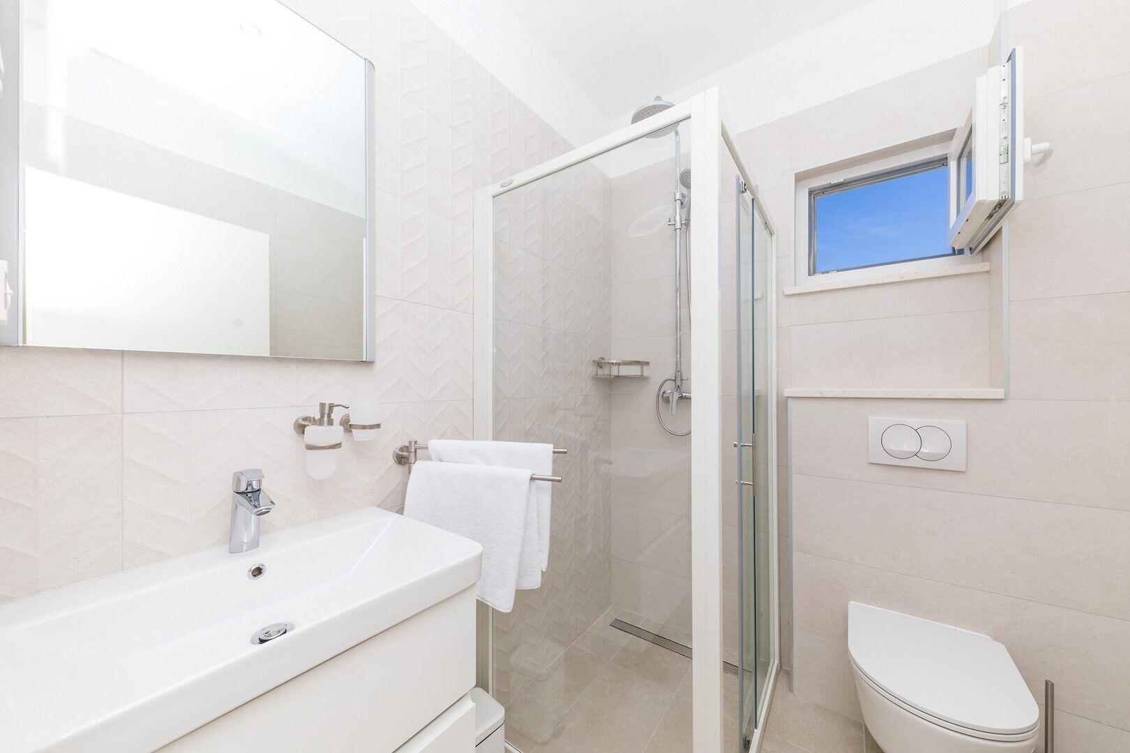 A modern bathroom with a large mirror, a white sink, a glass shower enclosure, and a toilet.