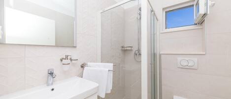 A modern bathroom with a large mirror, a white sink, a glass shower enclosure, and a toilet.