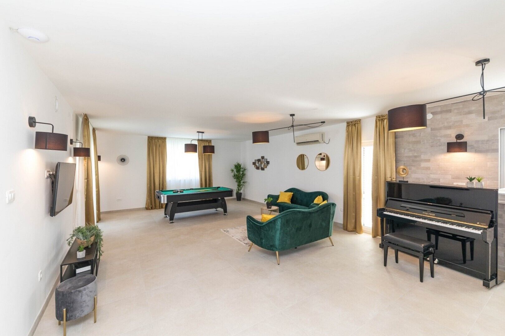 Un salon spacieux avec une table de billard, un canapé vert, un piano et un téléviseur.