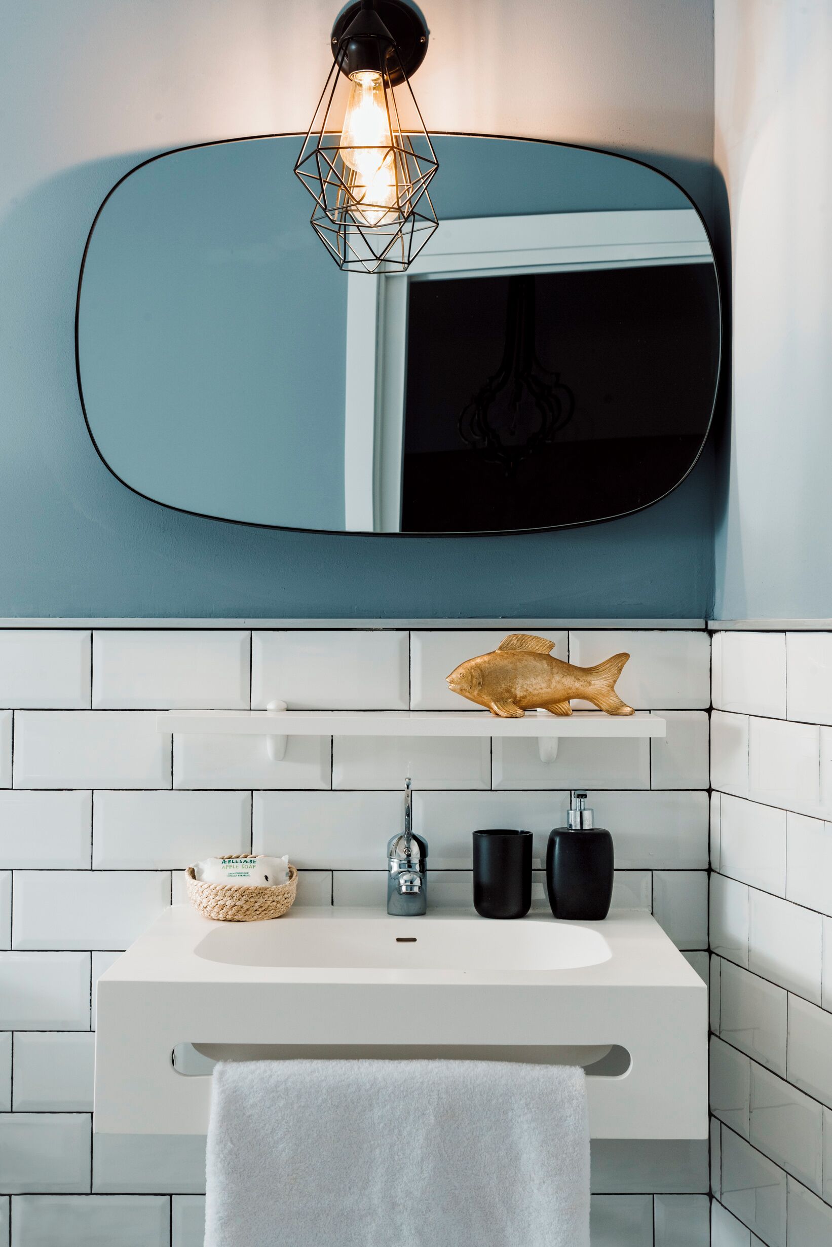 A modern bathroom with a white sink, a mirror, and a geometric light fixture.