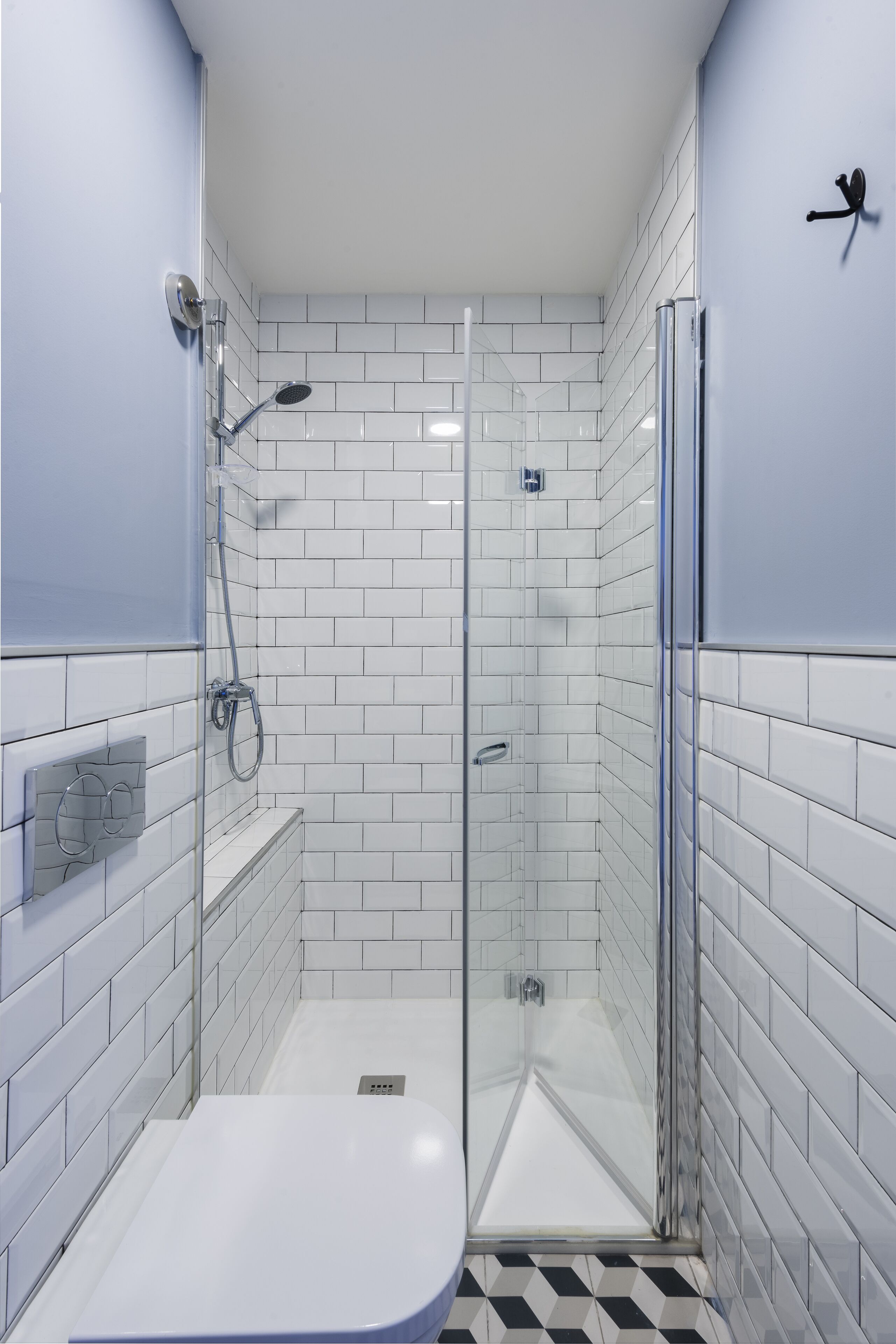 A modern bathroom with white subway tiles, a glass shower enclosure, and a black and white checkered floor.