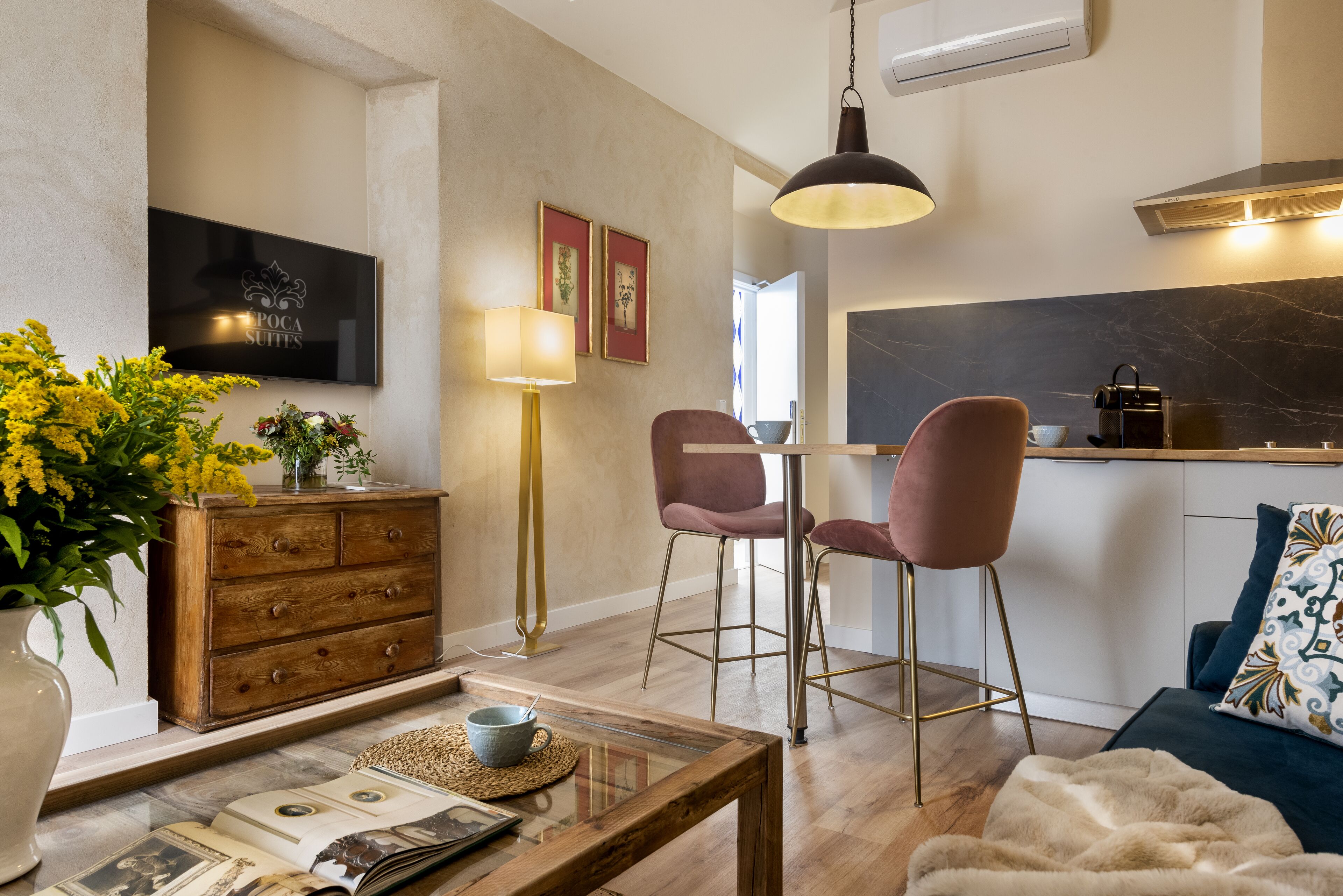 Una sala moderna con una mesa de centro de madera, un sofá, un televisor montado en la pared y una cocina con encimera de mármol.
