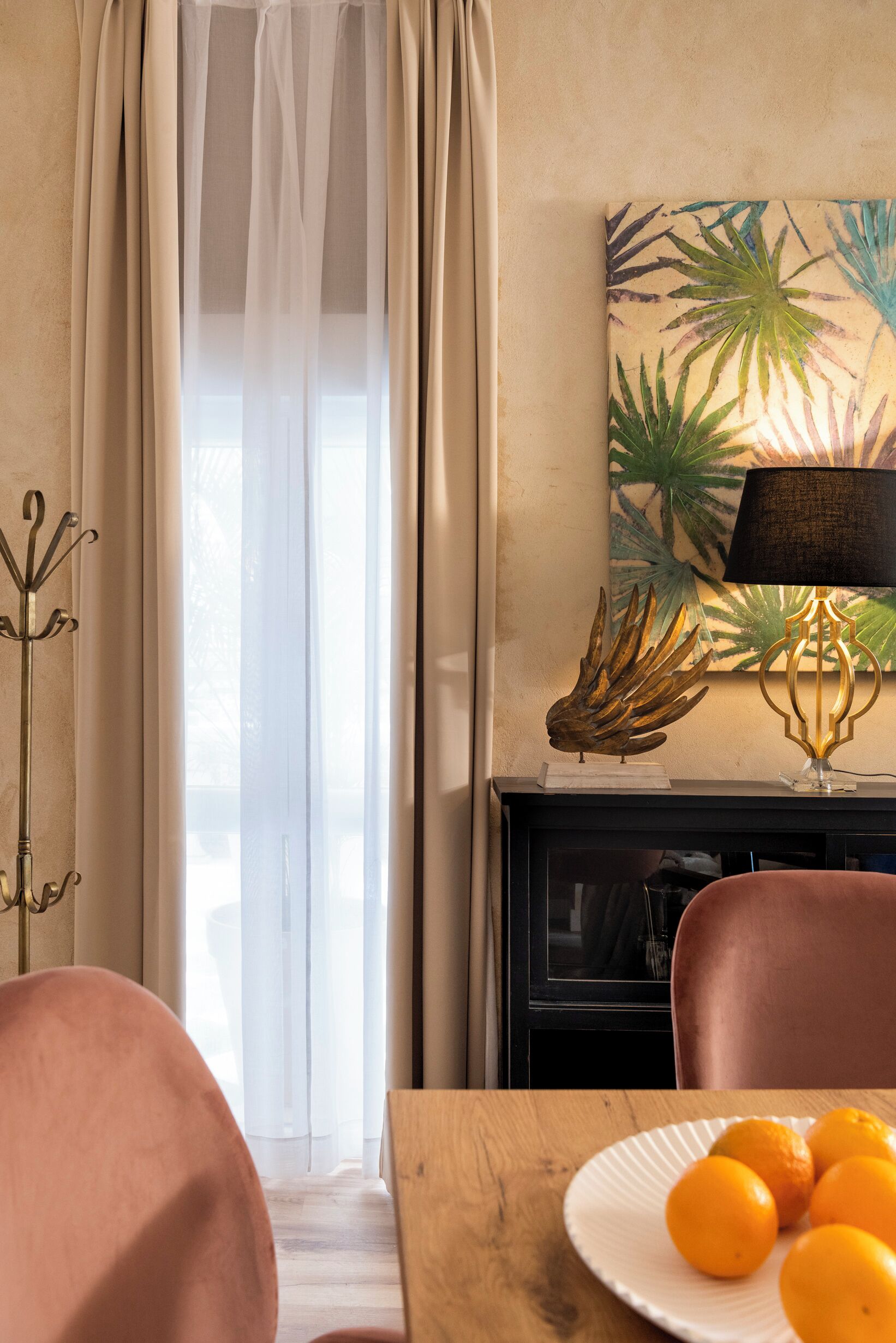 Une pièce avec une table à manger, une assiette d’oranges, une lampe et un tableau mural.