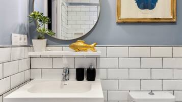 A bathroom with a white sink, a mirror, a toilet, and a framed plant on the wall.