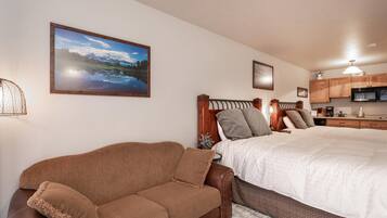 A bedroom with a bed, a brown leather sofa, a wooden headboard, and a kitchen area with wooden cabinets and a microwave.