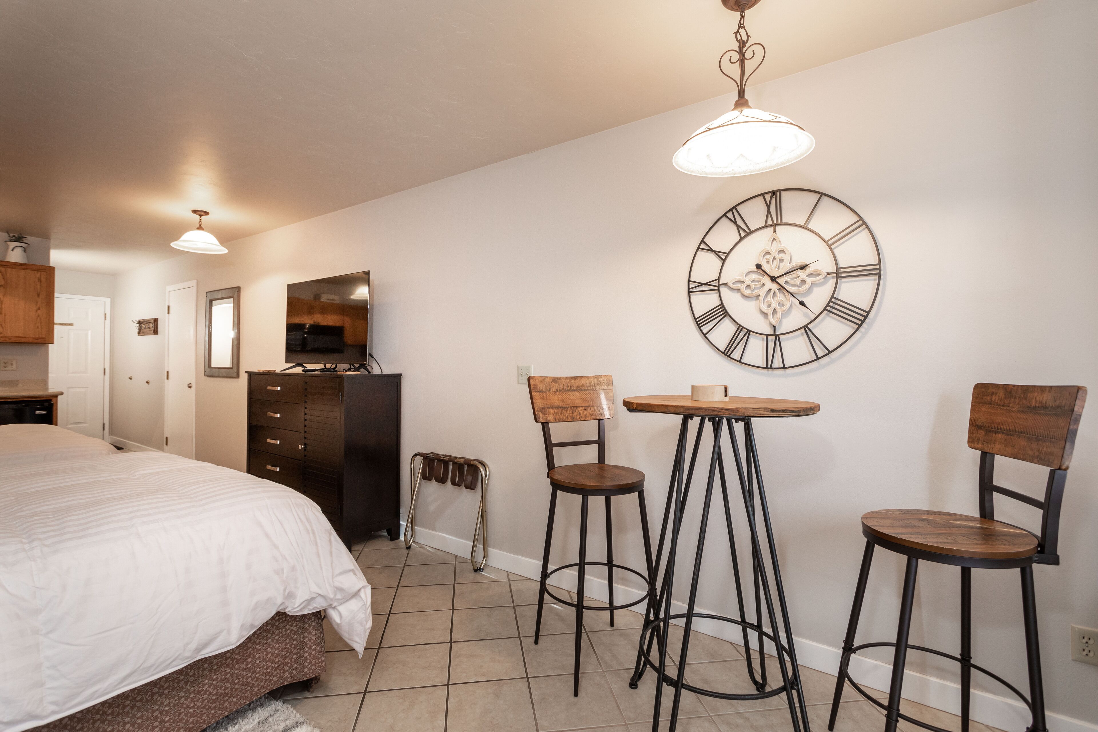 Quarto com cama, penteadeira, espelho e relógio de parede.