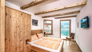 Quarto com cama de madeira, guarda-roupa de madeira, uma cadeira e televisão na parede.