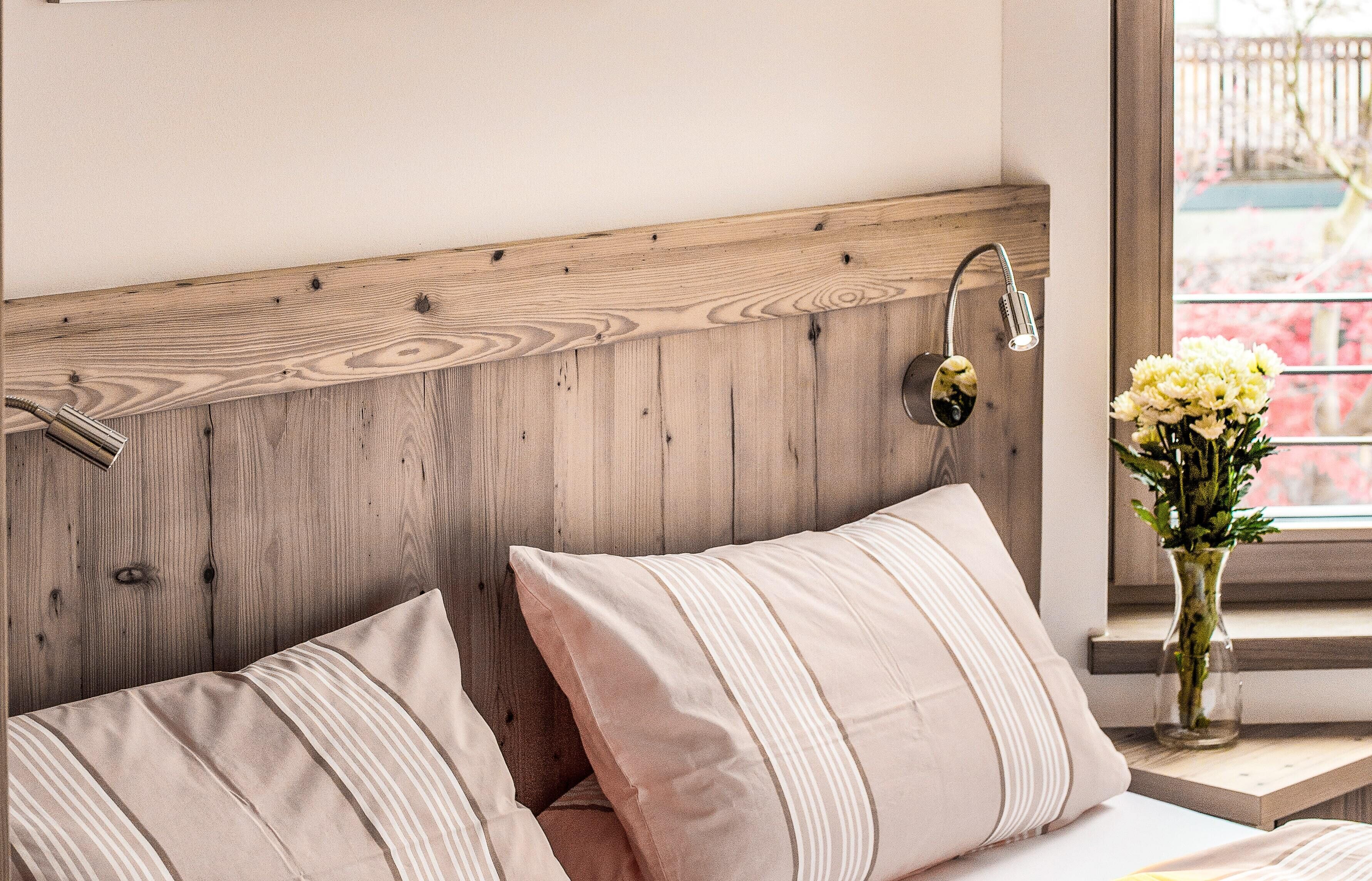 Un dormitorio con cabecera de madera, una mesita de noche con un florero y almohadas a rayas.