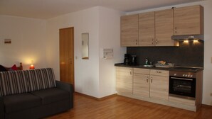 A compact living space with a kitchenette, a sofa, and a wooden door. - Pension & Ferienwohnung Breitmoser (Riedenburg)